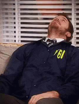 A Man Is Sleeping On A Couch Wearing A Fbi Jacket And Tie . GIF