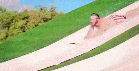 A Man Is Sliding Down A Water Slide In A Park . GIF