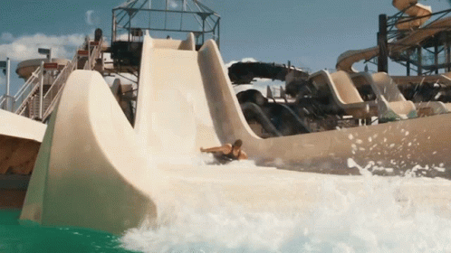 A Man Is Sliding Down A Water Slide In A Water Park GIF