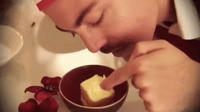 A Man Is Smelling A Piece Of Butter In A Bowl . GIF