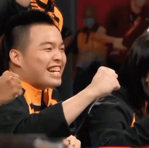 A Man Is Smiling And Holding His Fist In The Air While Sitting Next To A Woman . GIF