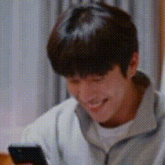 A Man Is Smiling And Looking At His Cell Phone . GIF