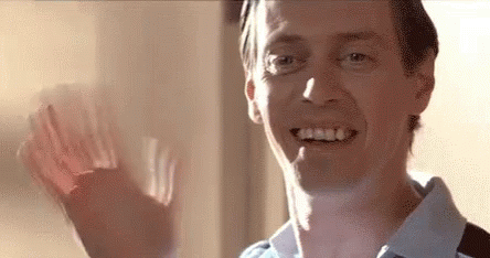 A Man Is Smiling And Waving His Hand In Front Of A Window . GIF