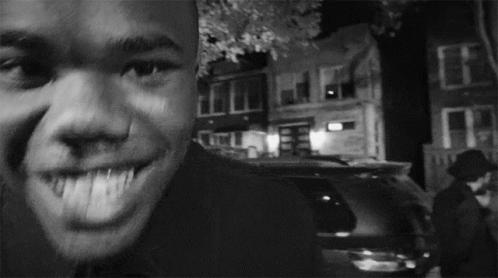 A Man Is Smiling In A Black And White Photo With A Car In The Background GIF