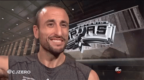 A Man Is Smiling In Front Of A Banner For The San Antonio Spurs GIF