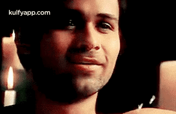 A Man Is Smiling In Front Of A Candle And Looking At The Camera . GIF