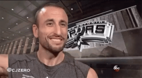A Man Is Smiling In Front Of A San Antonio Spurs Sign GIF