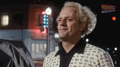 A Man Is Smiling In Front Of A Sign That Says Back To The Future On It GIF