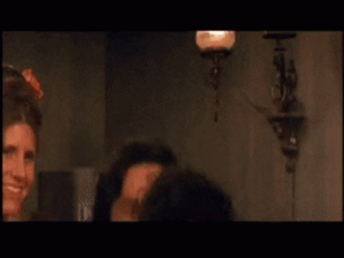 A Man Is Smiling In Front Of A Woman In A Room GIF
