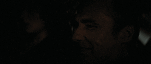 A Man Is Smiling In The Dark With A Woman In The Background GIF