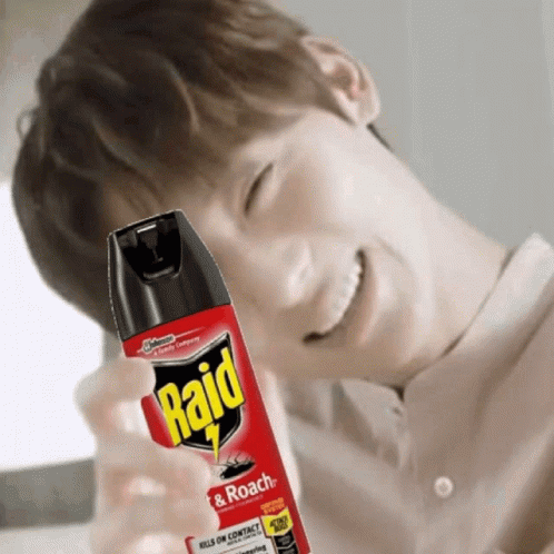 A Man Is Smiling While Holding A Bottle Of Raid Roach Spray GIF