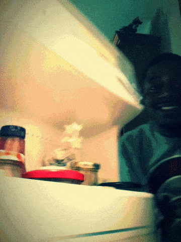 A Man Is Smiling While Looking Into A Refrigerator Filled With Jars Of Food GIF
