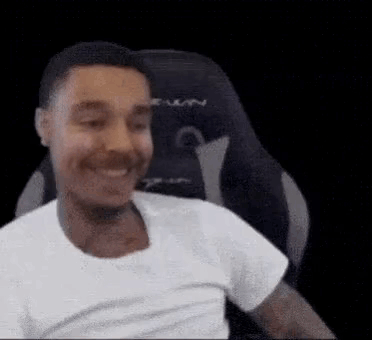 A Man Is Smiling While Sitting In A Gaming Chair . GIF