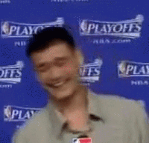 A Man Is Smiling While Standing In Front Of A Blue Wall That Says Playoffs . GIF