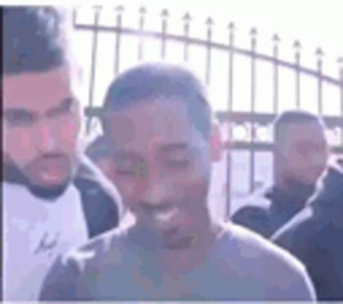 A Man Is Smiling While Standing In Front Of A Fence Surrounded By Other Men . GIF