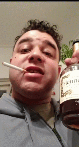 A Man Is Smoking A Cigarette And Holding A Bottle Of Hennessy Cognac GIF