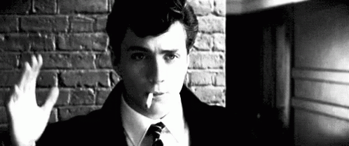 a man is smoking a cigarette in front of a brick wall .