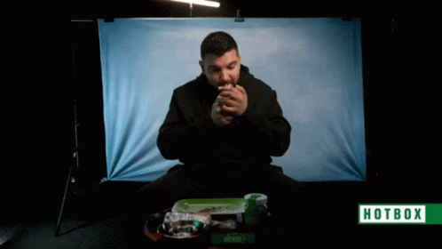 A Man Is Smoking A Cigarette In Front Of A Hotbox Banner GIF