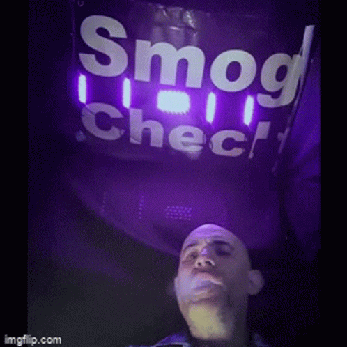 A Man Is Smoking A Cigarette Under A Sign That Says Smog Check GIF