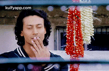 A Man Is Smoking A Cigarette While Looking Through A Window At Flowers . GIF