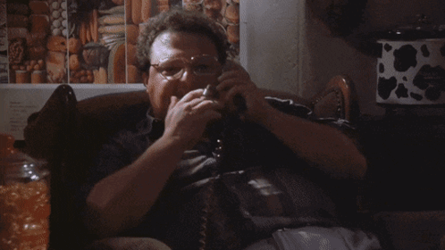 A Man Is Smoking A Cigarette While Talking On A Phone With The Word Excell Behind Him GIF