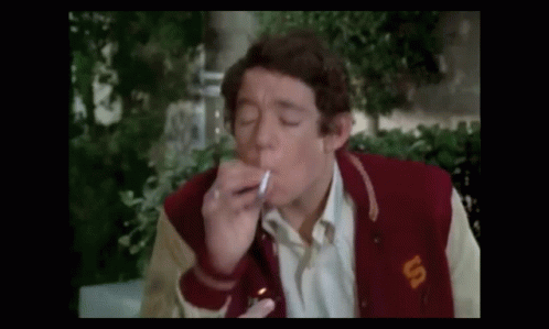 A Man Is Smoking A Cigarette While Wearing A Varsity Jacket . GIF