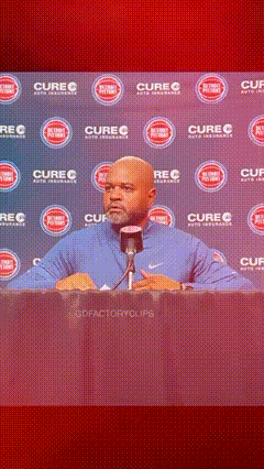 A Man Is Speaking Into A Microphone In Front Of A Wall That Says Cure GIF