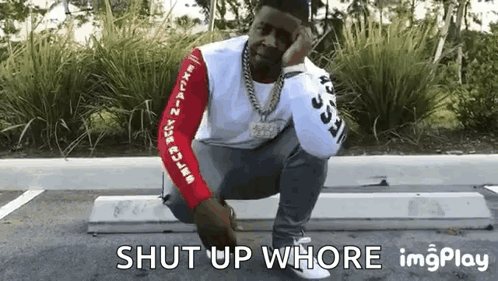 a man is squatting down in a parking lot with the words shut up whore written below him .