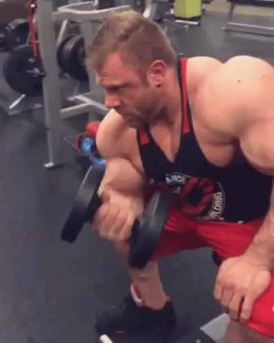 A Man Is Squatting Down While Holding A Dumbbell In His Hands In A Gym . GIF