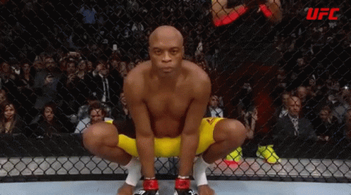 A Man Is Squatting In A Boxing Ring With A Crowd Watching . GIF