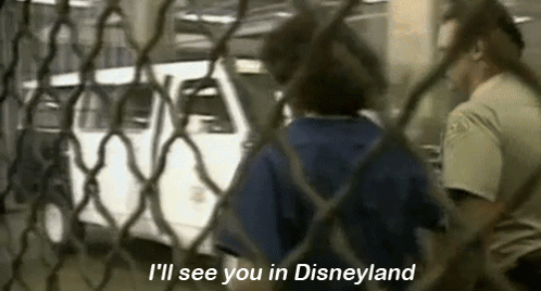 A Man Is Standing Behind A Chain Link Fence Talking To A Woman Behind It . GIF