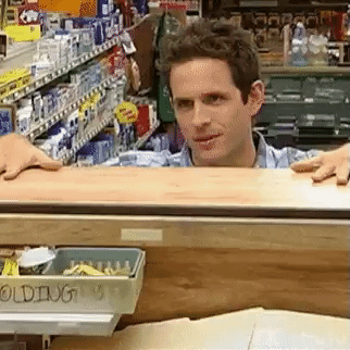 A Man Is Standing Behind A Counter In A Store Looking Over It . GIF