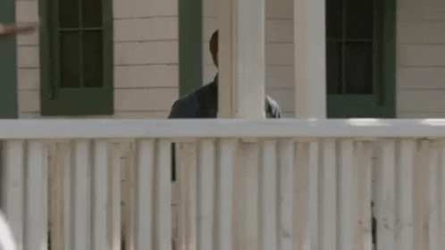 A Man Is Standing Behind A White Fence Looking Over It . GIF