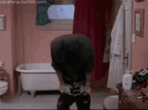 A Man Is Standing In A Bathroom With A Bathtub In The Background . GIF