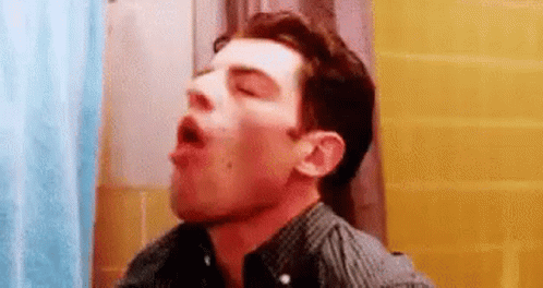 A Man Is Standing In A Bathroom With His Mouth Open And His Eyes Closed . GIF
