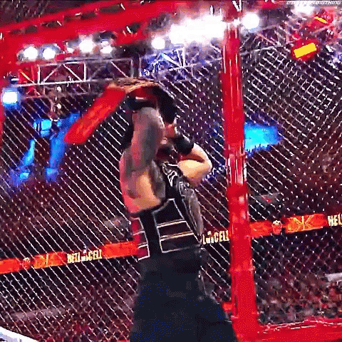 a man is standing in a cage holding a wrestling glove .