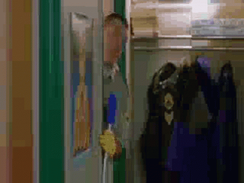 A Man Is Standing In A Closet Holding A Broom And Looking Out The Door . GIF