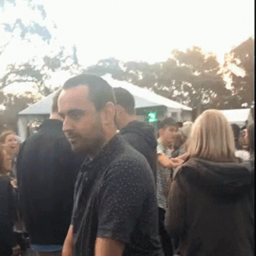 A Man Is Standing In A Crowd Of People With A Green Light In The Background GIF