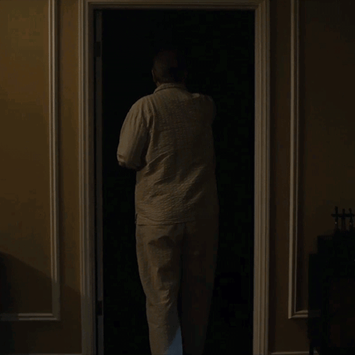 A Man Is Standing In A Dark Closet With A Lamp On GIF