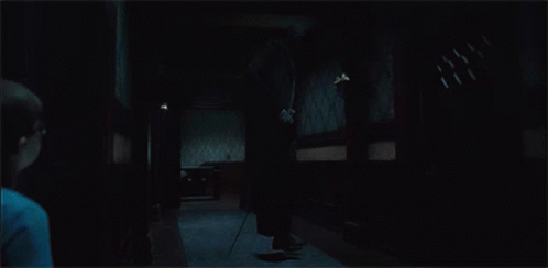 A Man Is Standing In A Dark Hallway Holding A Cane GIF