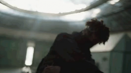 A Man Is Standing In A Dark Room With A Ceiling Light In The Background . GIF