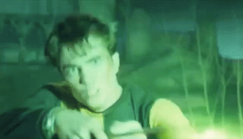 A Man Is Standing In A Dark Room With A Green Light Coming Out Of His Hand . GIF