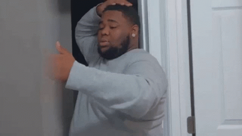 A Man Is Standing In A Doorway With His Hands On His Head . GIF