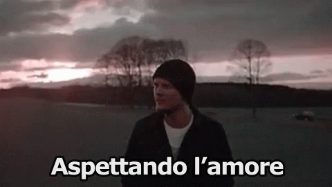A Man Is Standing In A Field With Trees In The Background And The Words Aspettando L ' Amore Above Him . GIF