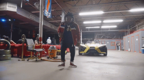 A Man Is Standing In A Garage With A Slingshot Car In The Background GIF