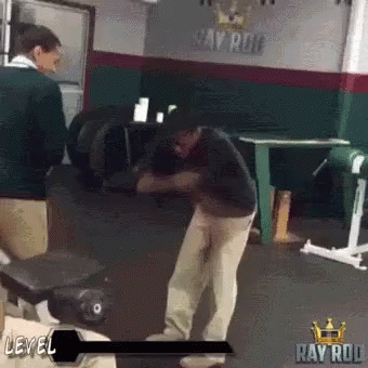 A Man Is Standing In A Gym In Front Of A Sign That Says Ray Rod . GIF