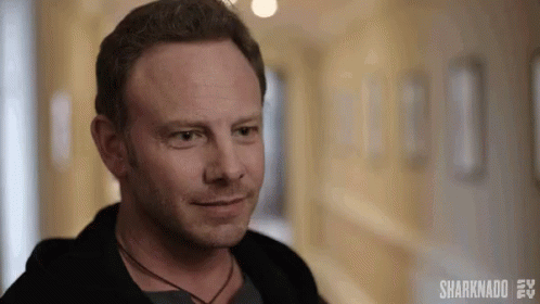 A Man Is Standing In A Hallway Smiling And Looking At The Camera . GIF