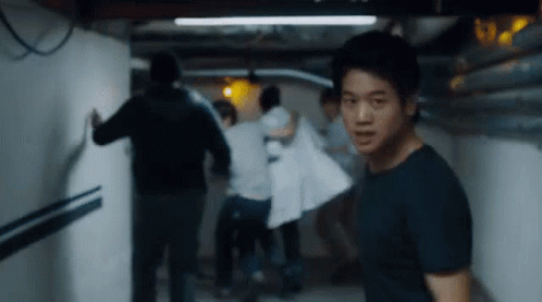 A Man Is Standing In A Hallway With A Group Of People . GIF