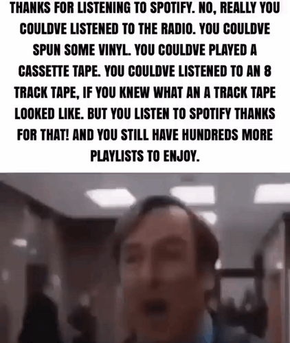 A Man Is Standing In A Hallway With A Spotify Playlist On His Phone . GIF