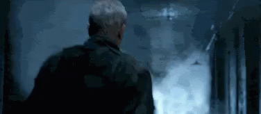 A Man Is Standing In A Hallway With Smoke Coming Out Of The Door . GIF